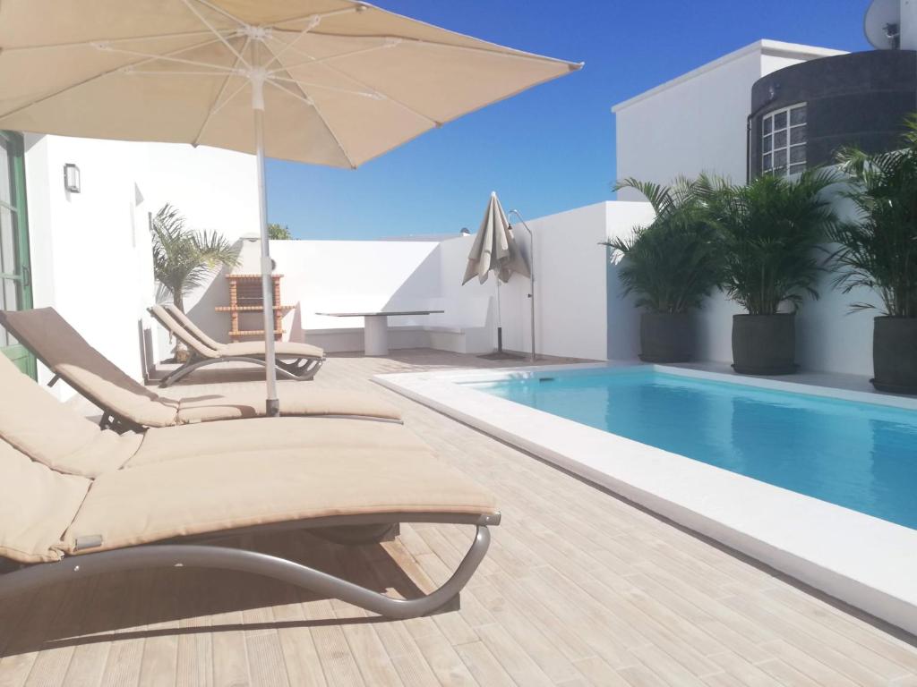 a swimming pool with two lounge chairs and an umbrella at Villa Elena in Puerto del Carmen