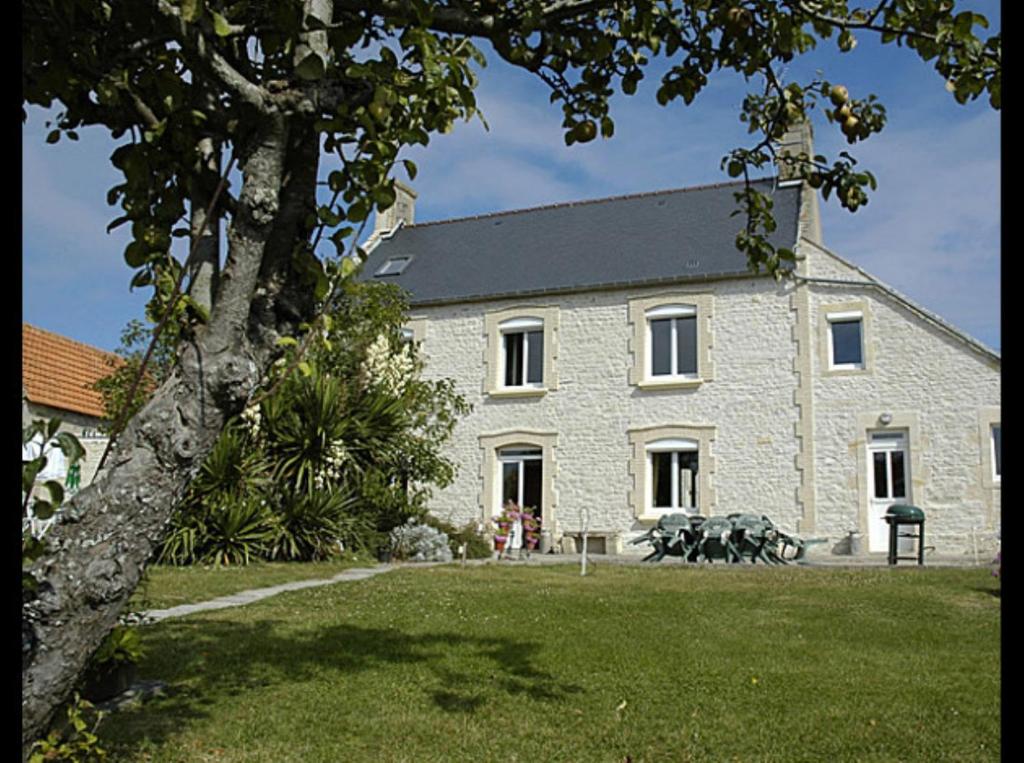 ein großes Steingebäude mit einem Baum davor in der Unterkunft Maryse et Jean-Pierre in Longues-sur-Mer