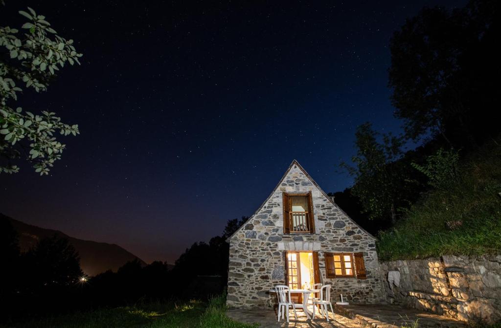 a stone house with a window and chairs at night at Granges Bergeries Chalets de LAS COSTES insolites en forêt à Loudenvielle 4X4 recommandé l'hiver à 2km des remontées mécaniques in Loudenvielle