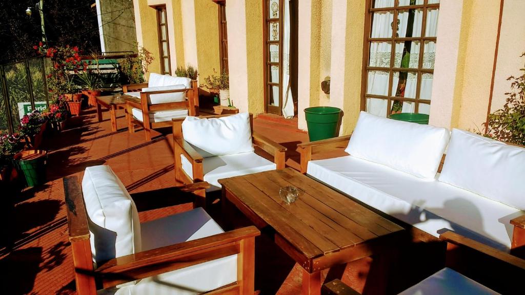 a porch with wooden tables and white couches and chairs at Posada del Buscador in El Bolsón