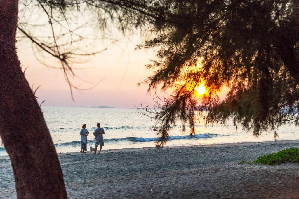 two people and a dog on the beach at sunset at Family-friendly house, a few steps from the pool and close to the ocean. in Mae Pim