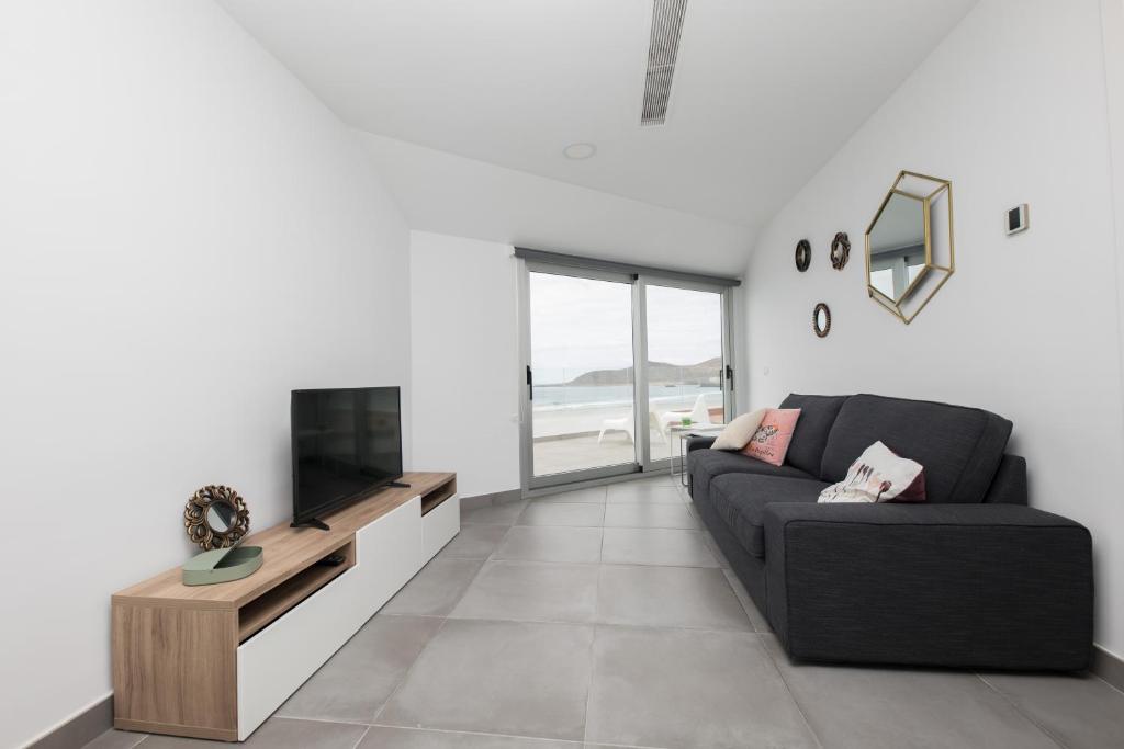 sala de estar con sofá negro y TV en Fantástico ático en primera línea de playa, en Las Palmas de Gran Canaria