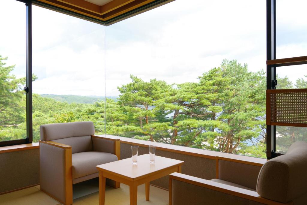a room with a chair and a table and large windows at Jodogahama Park Hotel in Miyako
