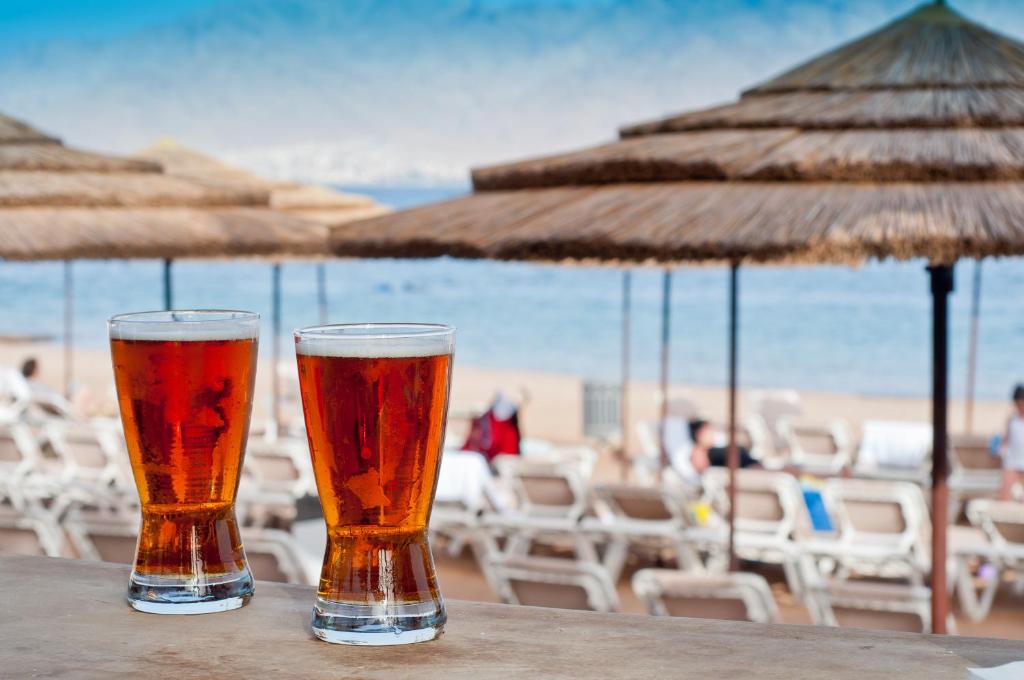 zwei Gläser Bier auf einem Tisch am Strand in der Unterkunft U Coral Beach Club Eilat – Ultra All inclusive in Eilat