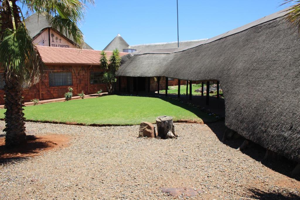ein Gebäude mit einem Grasdach und einem Hof in der Unterkunft Kalahari Lodge Kimberley in Kimberley