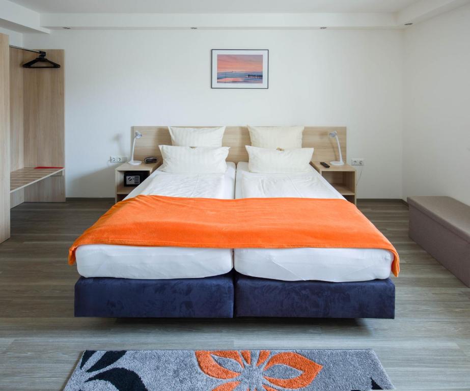 a bedroom with a large bed with an orange blanket at Hotel Moerser Hof in Moers