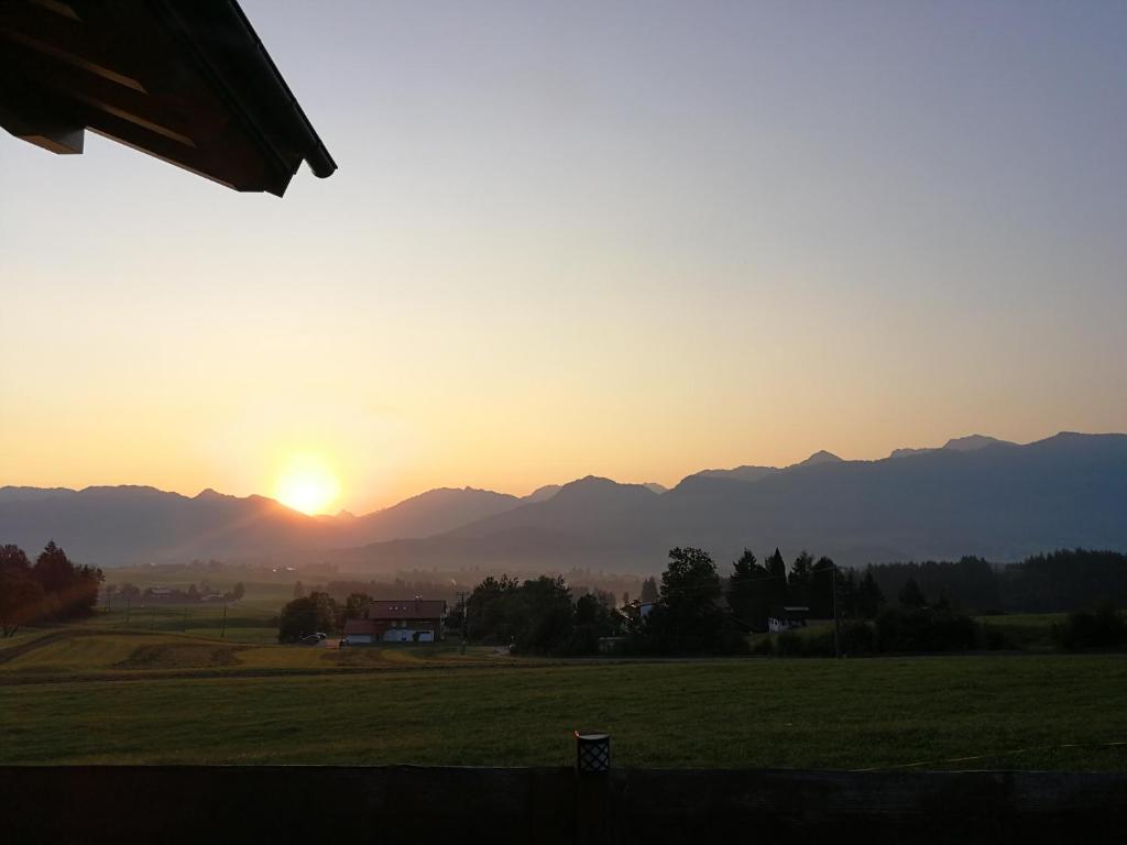 una puesta de sol sobre un campo con montañas en el fondo en Ferienwohnung Greif, en Ofterschwang