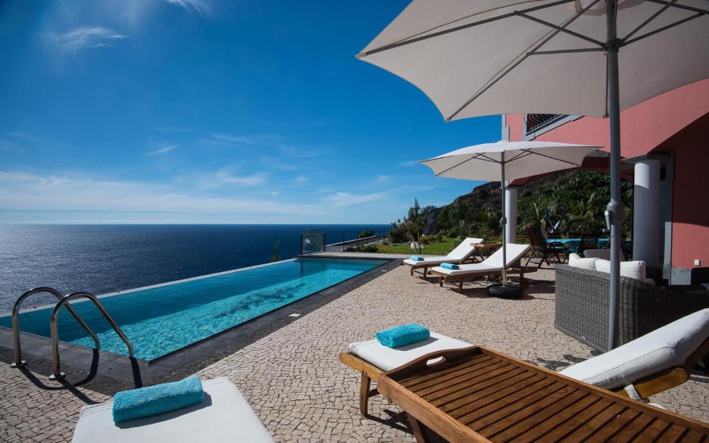ein Pool mit Stühlen und einem Sonnenschirm und das Meer in der Unterkunft Luxury Ocean Front Villla in Calheta