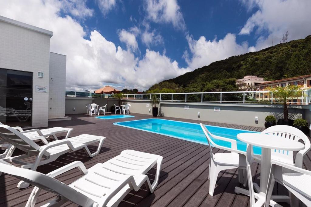 eine Terrasse mit weißen Stühlen und einem Pool in der Unterkunft Hotel Rosenbrock in Balneário Camboriú