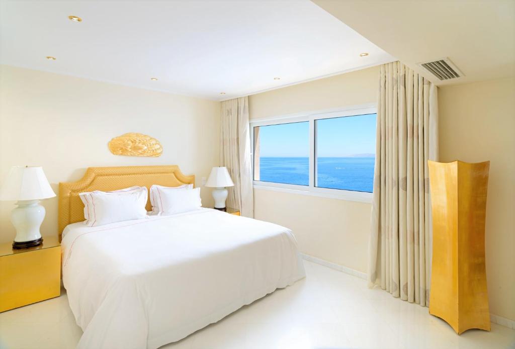 a white bedroom with a large bed and a large window at Out Of The Blue Resort & Spa in Agia Pelagia