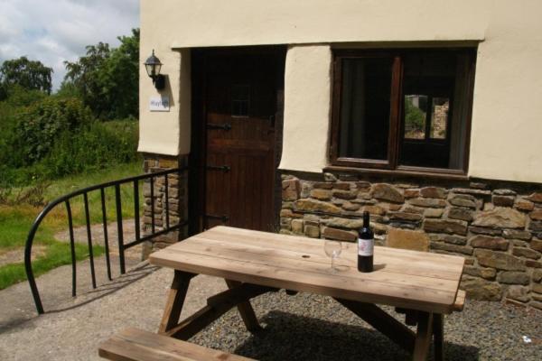 a wooden picnic table with a bottle of wine on it at Hayloft Cottage in Merton