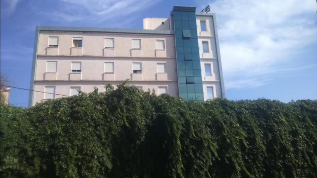 a tall white building behind a hedge at Roza Hotel in Bab Ezzouar