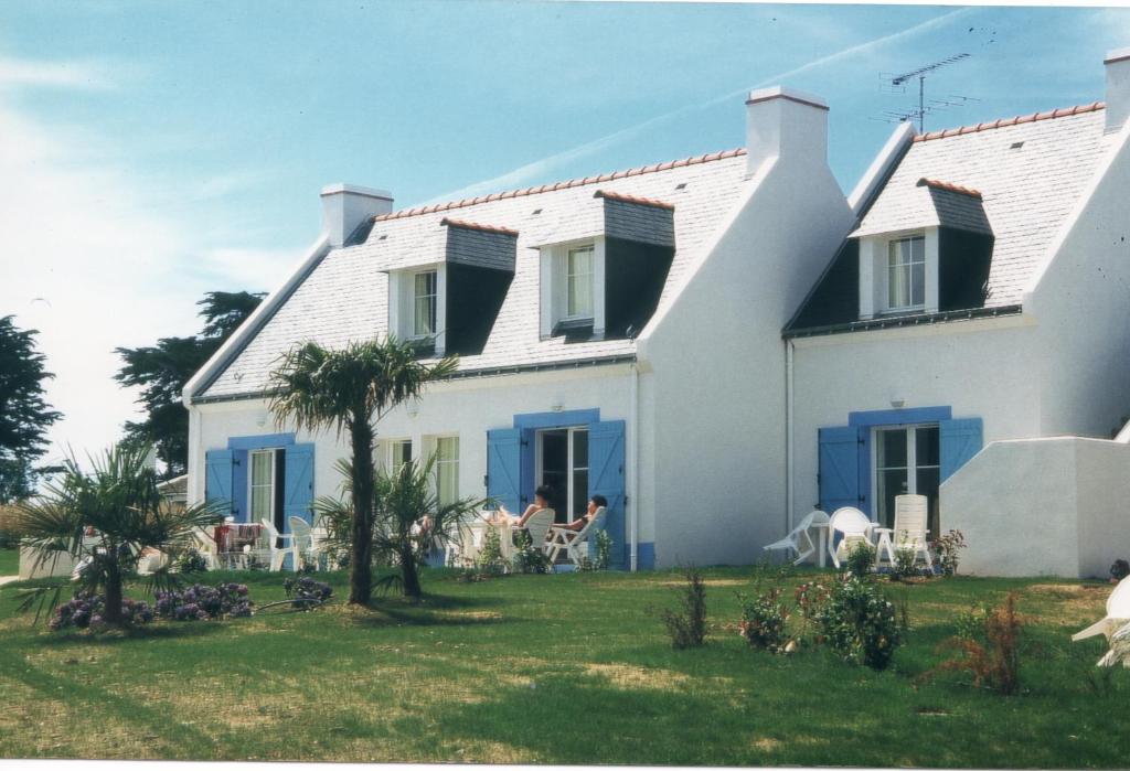 a white house with blue shutters on a yard at Résidence Marie Galante Locmaria avec piscine in Locmaria