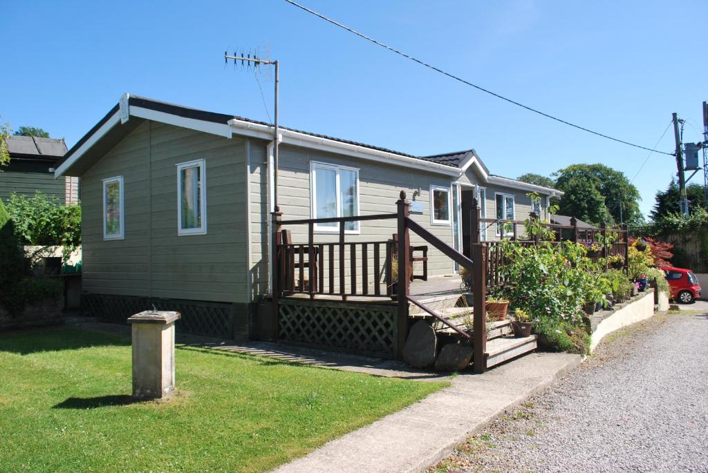 a small green house with a large wooden deck at Natland Caravan Park in Kendal