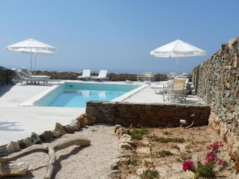 a swimming pool with umbrellas and a stone wall at Lithia Villas in Chora Folegandros
