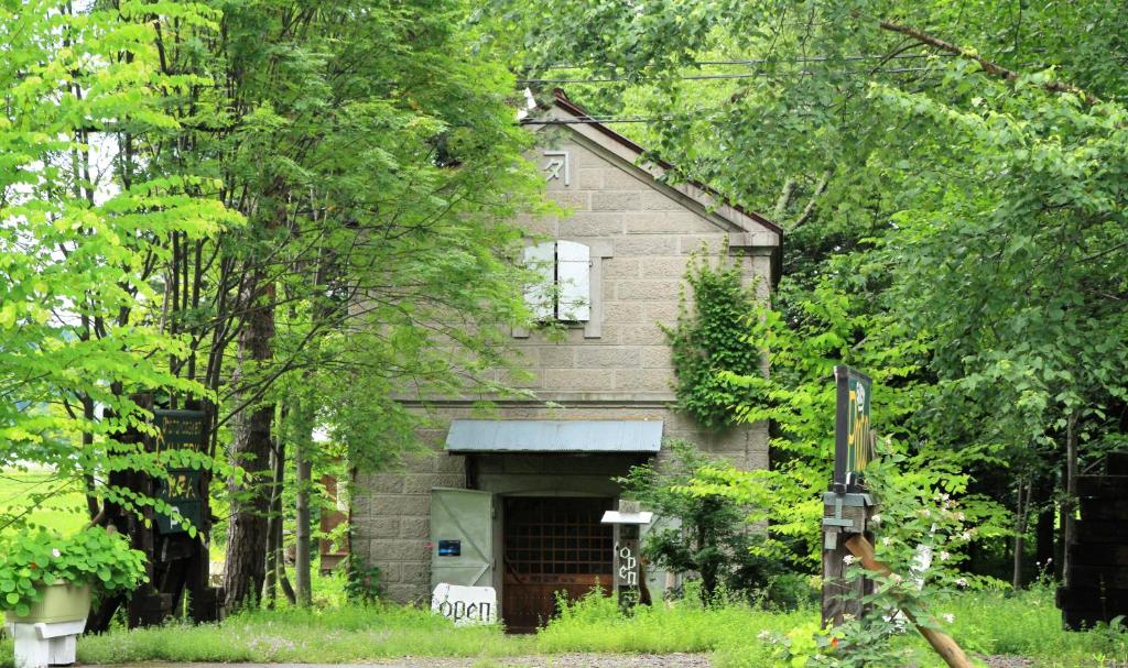 una vieja casa de ladrillo con un garaje en el bosque en Gallery Stay Kitashajin en Higashikawa