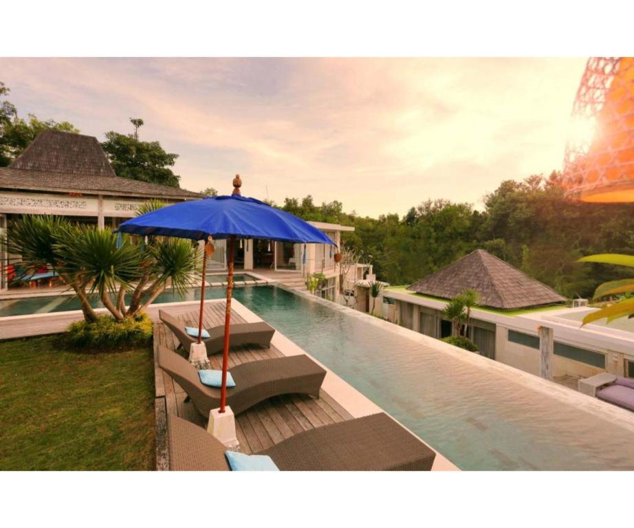 a pool with a blue umbrella and benches next to a house at Sunset Paradise Villa Uluwatu in Uluwatu