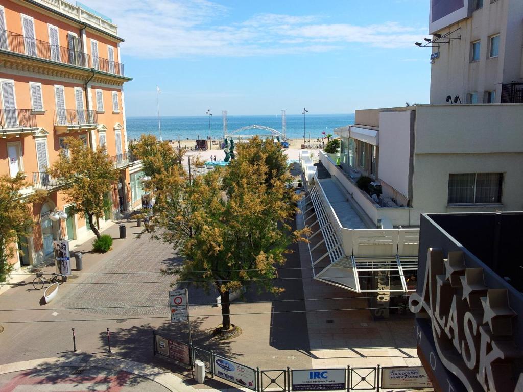 uma rua da cidade com edifícios e o oceano no fundo em Hotel Garni' Alaska em Riccione