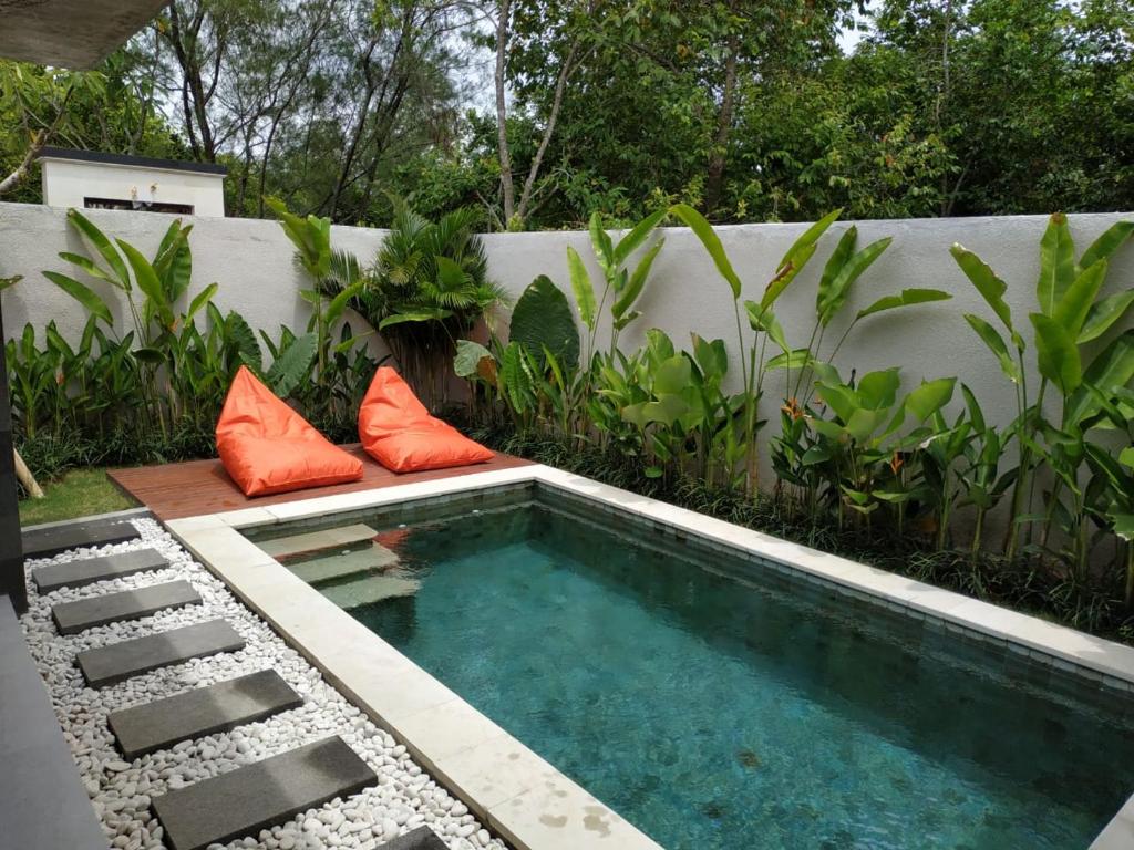ein kleiner Swimmingpool mit orangefarbenen Kissen neben einem Zaun in der Unterkunft La Isla Villas Bali in Canggu