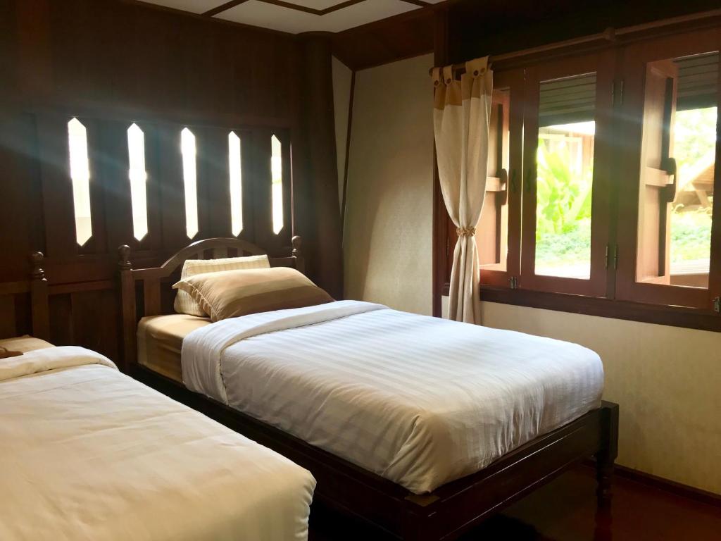 two beds in a bedroom with two windows at Kawila126 in Chiang Mai