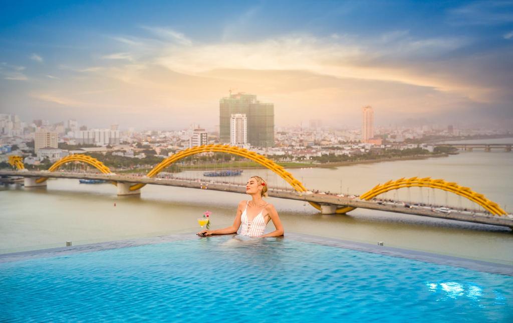 a woman sitting in a infinity pool with a bridge at Val Soleil Hotel in Da Nang