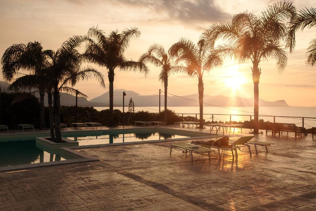 a resort with a pool and palm trees and the sunset at Petruso Resort in Balestrate