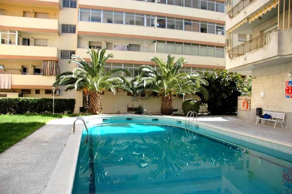 a swimming pool in front of a building with palm trees at Apartamentos Indasol in Salou