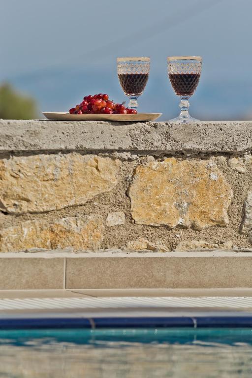 two glasses of wine on a wall next to a pool at Kalimera Karpathos Exclusive Villas in Afiartis