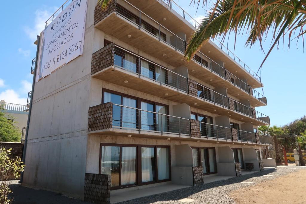 a building with a balcony and a palm tree at Departamentos Kudun in Pichilemu