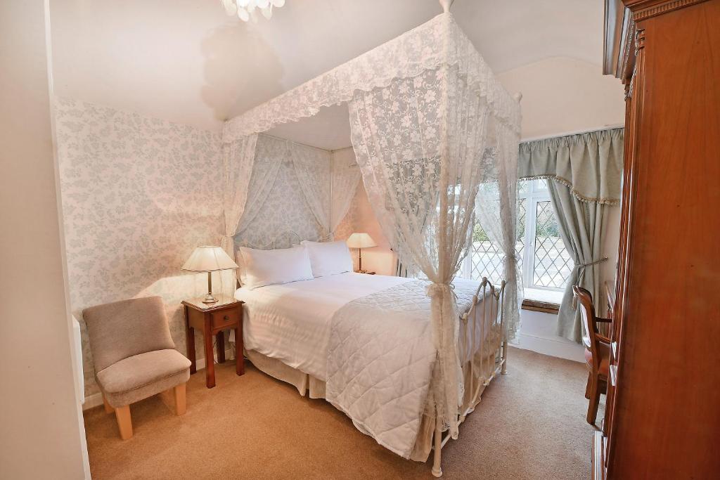 - une chambre avec un lit à baldaquin et une chaise dans l'établissement Virginia Lodge, à Stratford-upon-Avon
