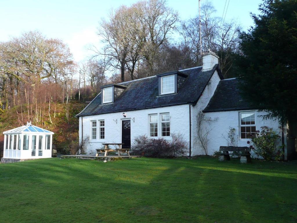 a white house with a picnic table in a yard at Dubh Loch Cottage in Rowardennan