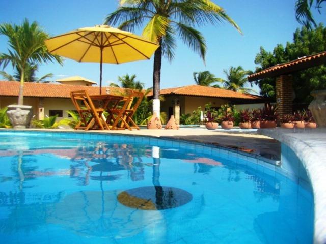 a swimming pool with a table and an umbrella at Pousada Casa Dona Rosa in Cumbuco