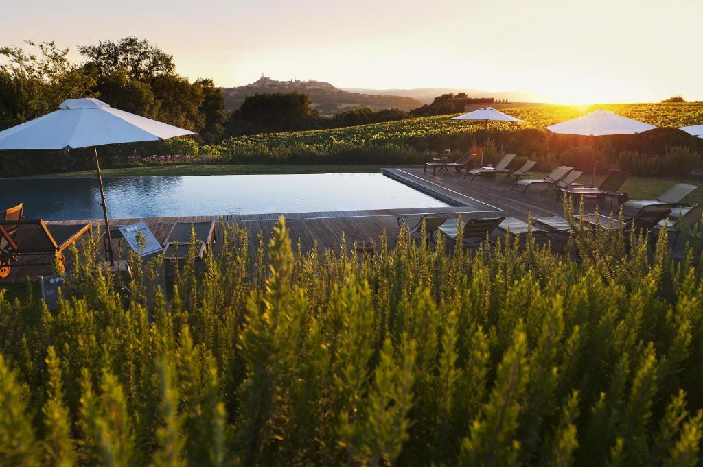 a pool with chairs and umbrellas next to a lake at Roccafiore Spa & Resort in Todi