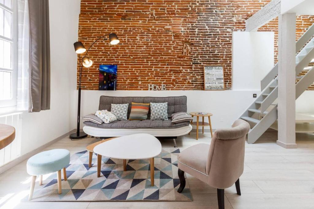 a living room with a couch and chairs and a brick wall at ❤️ Charmant appart ancien rénové place des Carmes in Toulouse