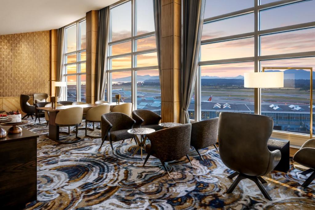 Fairmont Gold at Fairmont Vancouver Airport في ريتشموند: لوبي الفندق مع الكراسي والطاولات والنوافذ الكبيرة