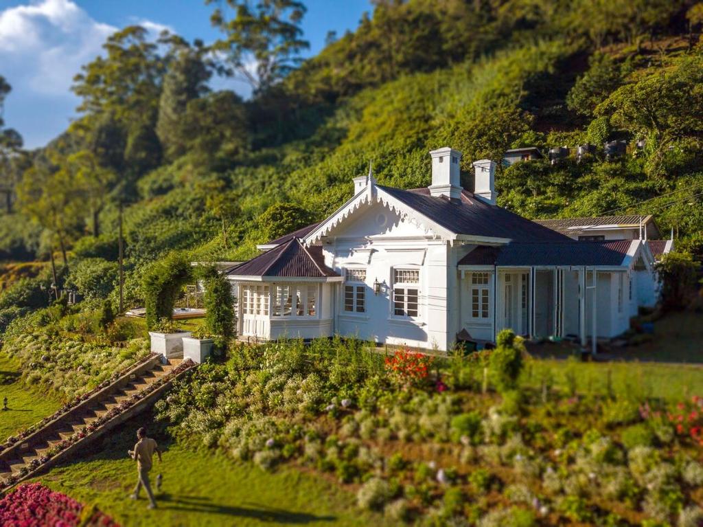 a white house on a hill with a man standing in front of it at The Clovelly Bungalow in Nuwara Eliya