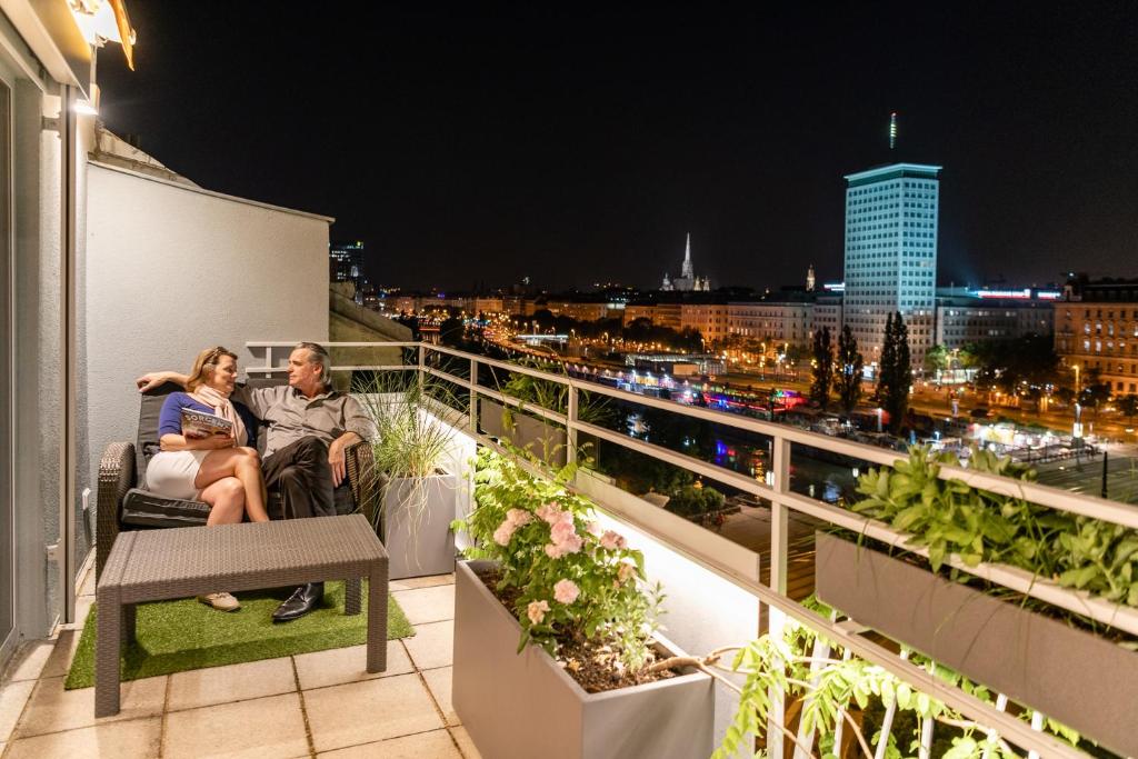 Skyflats Vienna Ring View في فيينا: رجل وامرأة يجلسان في الشرفة في الليل