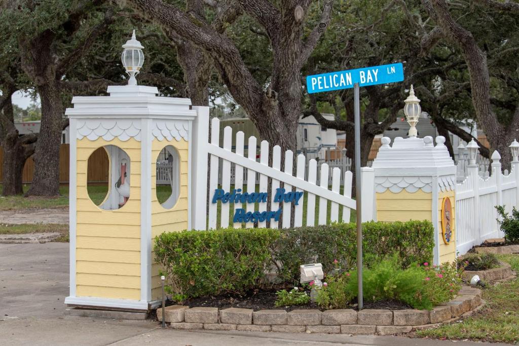 a white fence with a yellow house and a street sign at D&R Pelican Bay Resort in Rockport