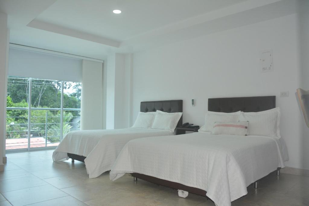 two beds with white sheets in a white room at Towers100 Aparta Estudios in Apartadó