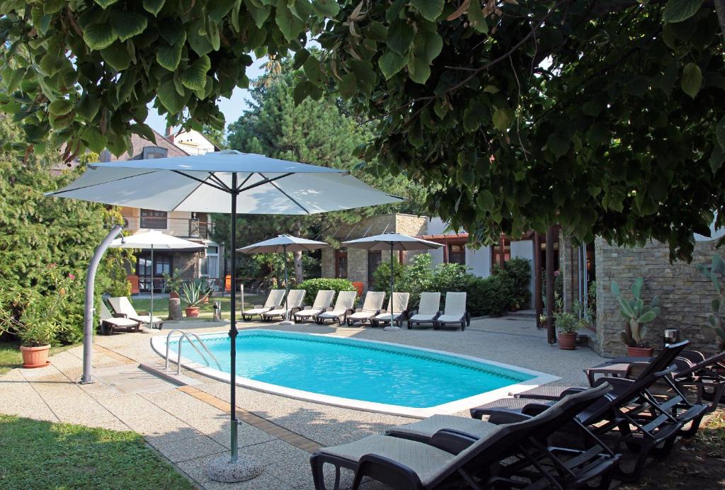 uma piscina com cadeiras e um guarda-sol ao lado em Adler Hotel & Wellness em Tihany