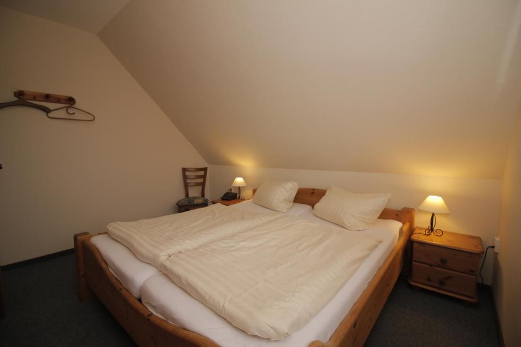 - une chambre avec un lit avec des draps blancs et 2 lampes dans l'établissement Strandroggen, à Wangerland