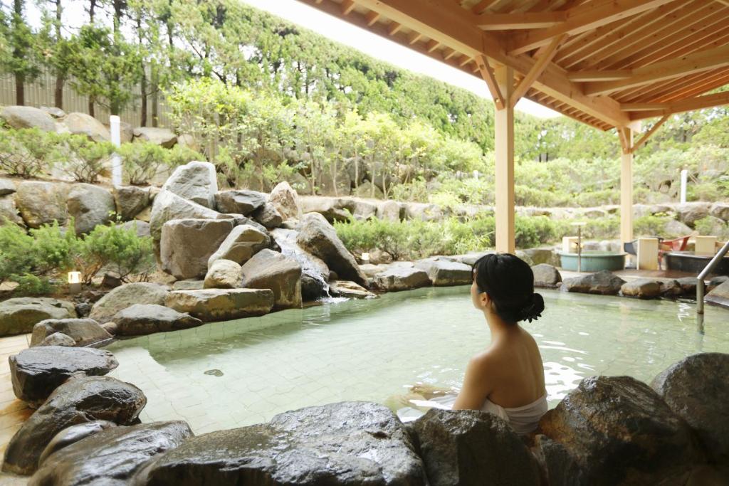 a woman sitting in a pool of water with rocks at Kyukamura Noto-Chirihama in Hakui
