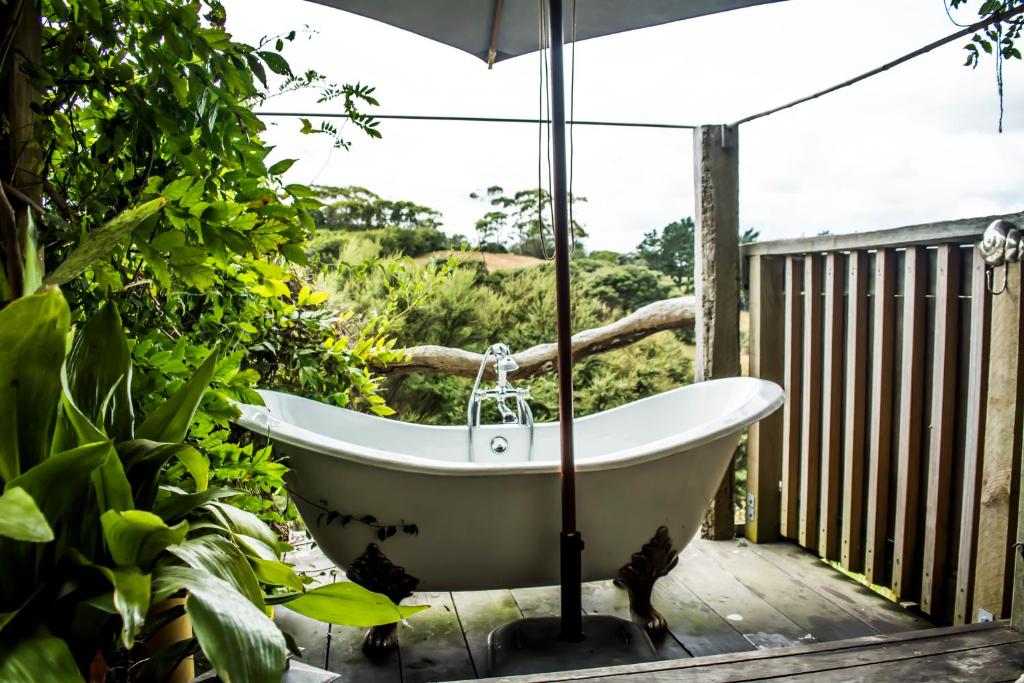 a bath tub on a deck with an umbrella at Freshwaterfarm Cottages - Muriwai in Waimauku