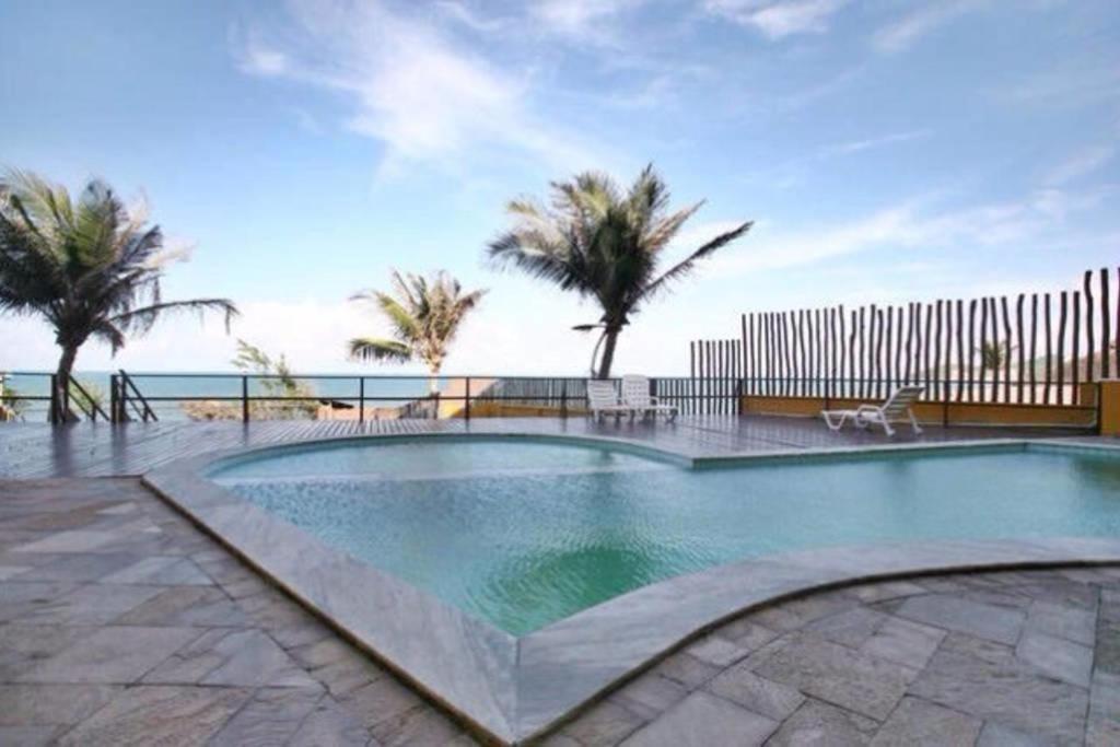 a swimming pool with palm trees and the ocean at Atlântico Flat Apto 103 in Natal