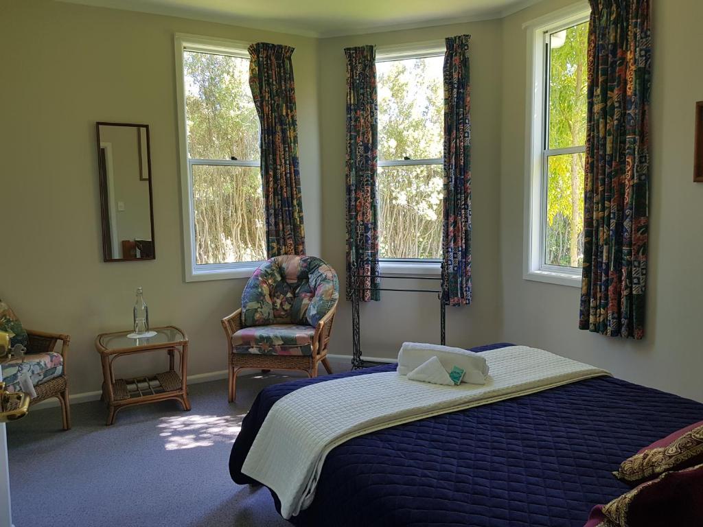 a bedroom with a bed and a chair and windows at Lancewood Lodge in Bulls