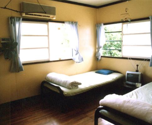 a small room with a bed and two windows at Minshuku Rakutenya in Ishigaki Island