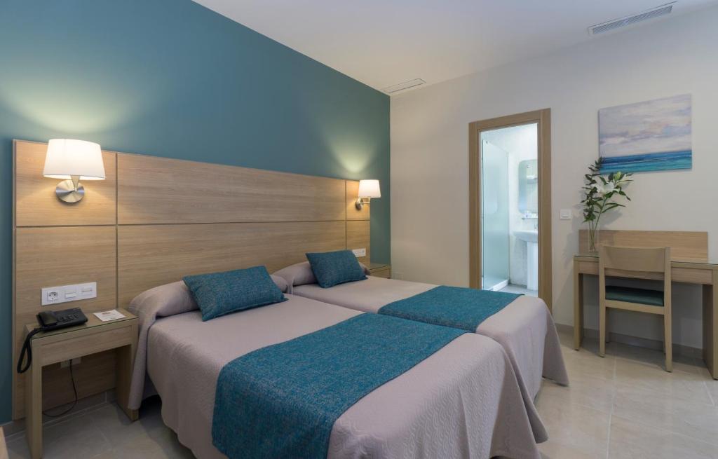 a bedroom with two beds and a table with a desk at Hotel Sur Málaga in Málaga