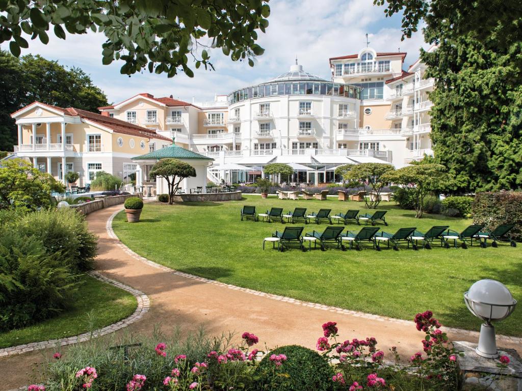 ein großes weißes Gebäude mit Stühlen in einem Park in der Unterkunft Travel Charme Strandidyll Heringsdorf in Heringsdorf