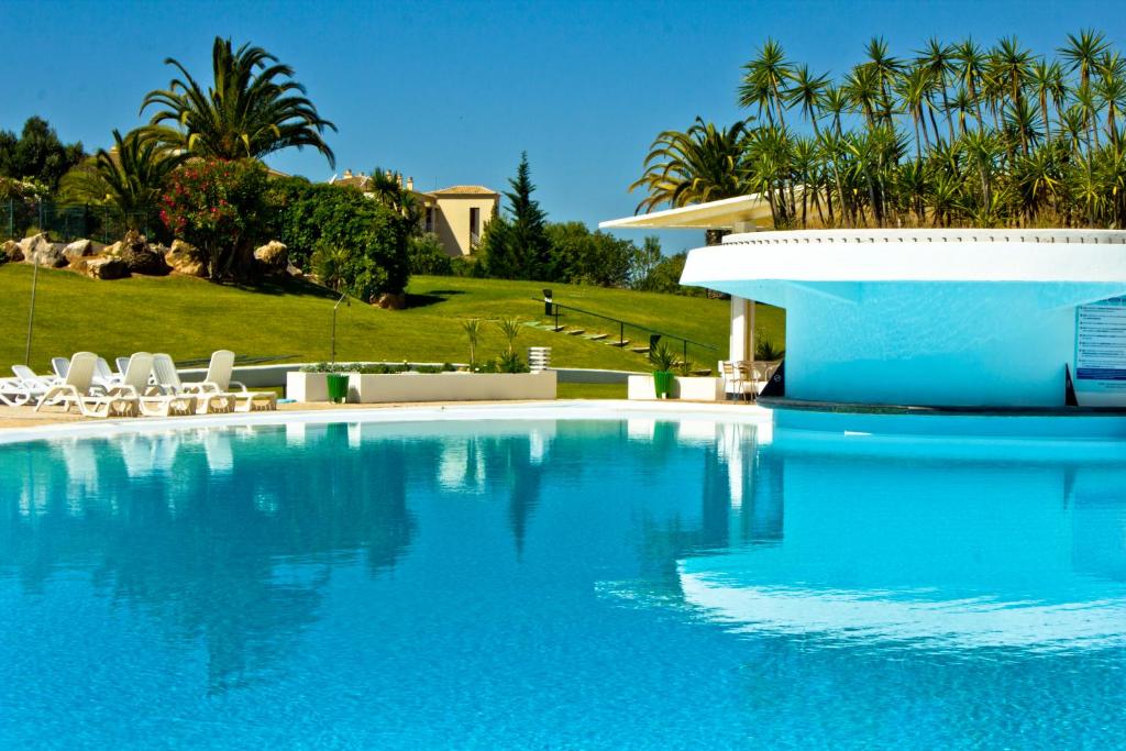 a blue swimming pool with white chairs and palm trees at Vila Marachique Torralvor in Alvor