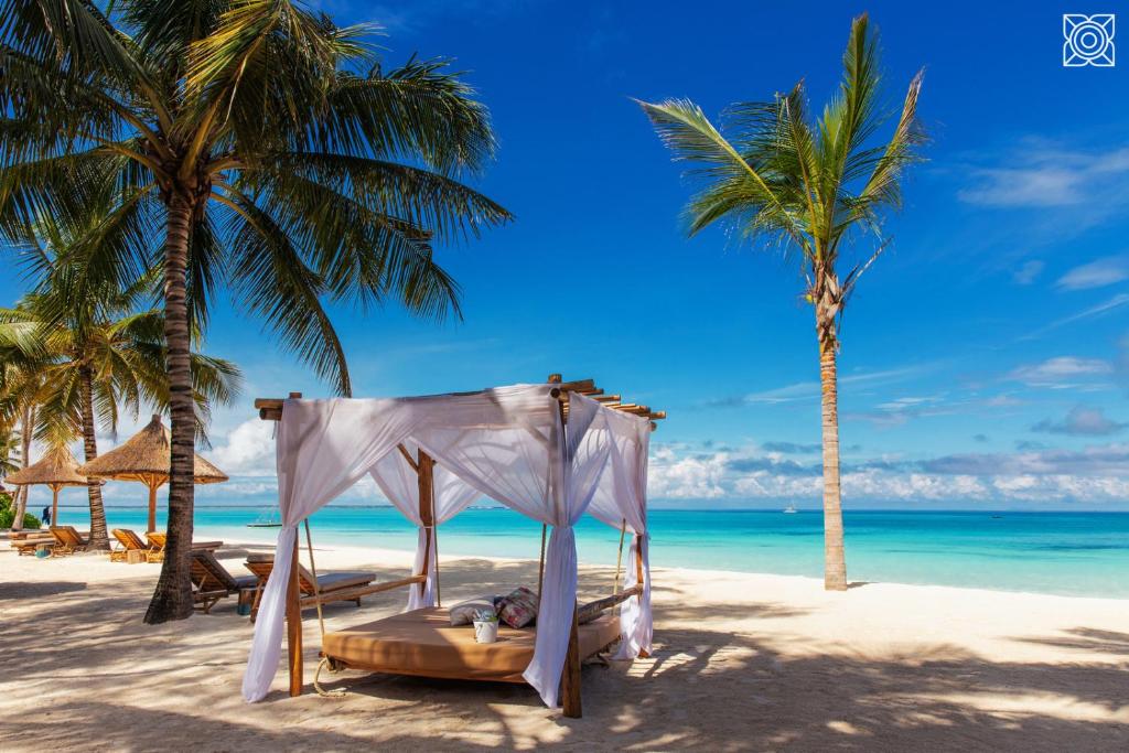 a bed on a beach with two palm trees at Zuri Zanzibar in Kendwa